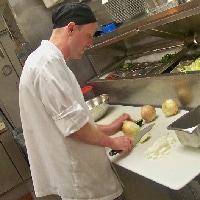 David Meloy, Marketing and Community Relations Manager, working as a lead cook (chopping onions) in a kitchen in 2012