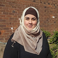 Woman stands in front of a brick wall with a tan burka