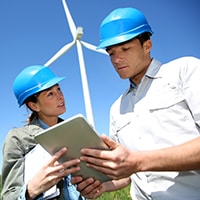 Two people in hard hats standing in front of a wind turbine