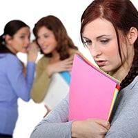 Two women in the background whisper among themselves while one woman in the foreground clutches a folder with papers to her chest with a sullen look on her face